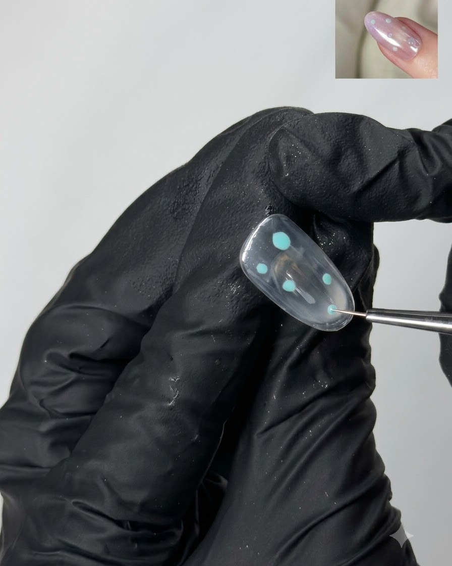 A fine detailing brush placing small turquoise dot accents onto a clear gel nail surface.