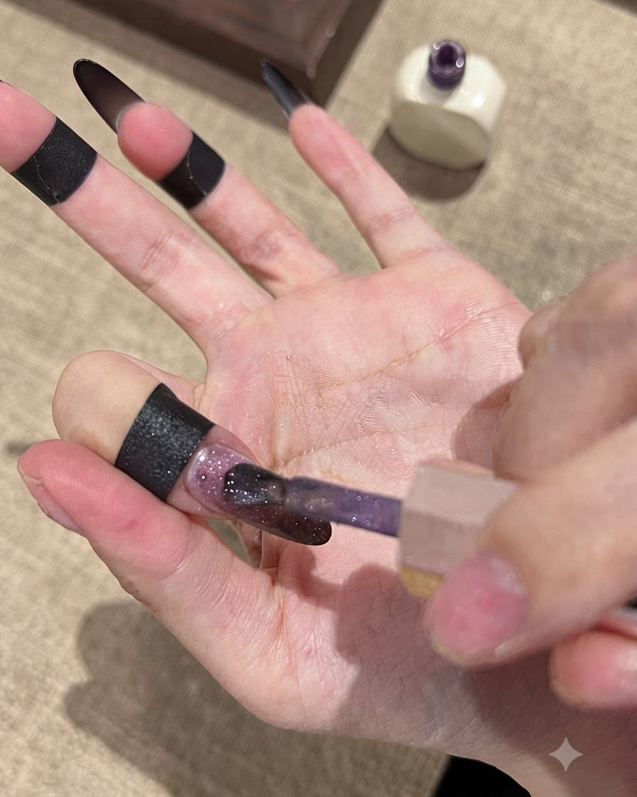 A brush applying Fallen Gold Cat Eye gel polish over a dark gradient nail base.