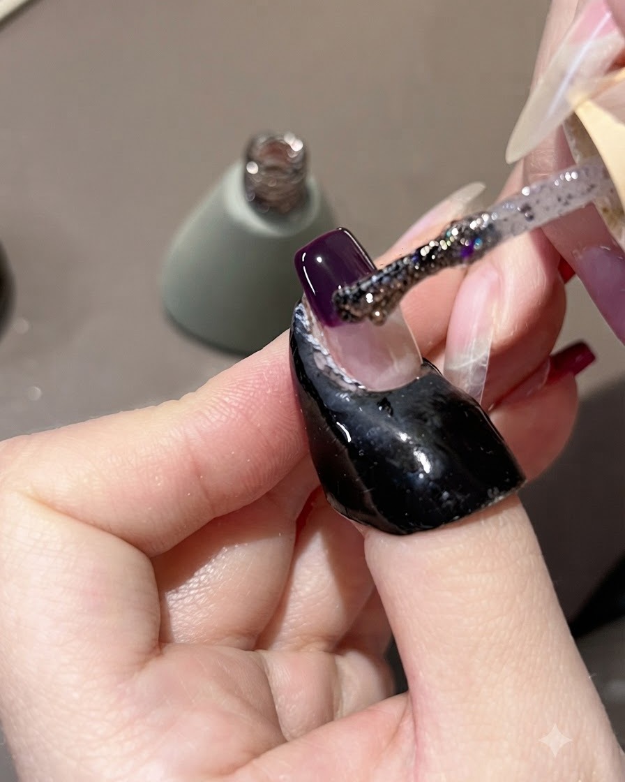 A brush applying purple glitter gel over a dark purple nail tip, pulling it slightly upward.