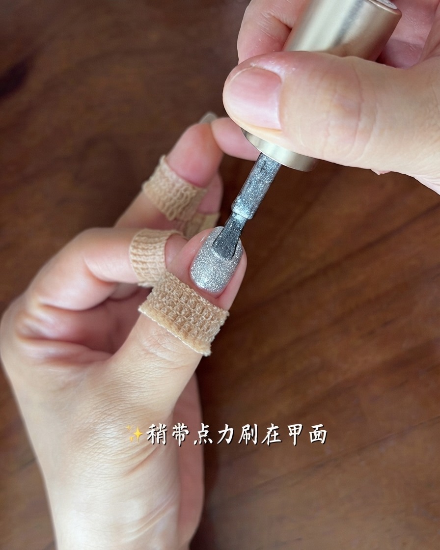 A brush applying a thin, sparkling layer of silver-grey cat eye gel onto a fingernail.