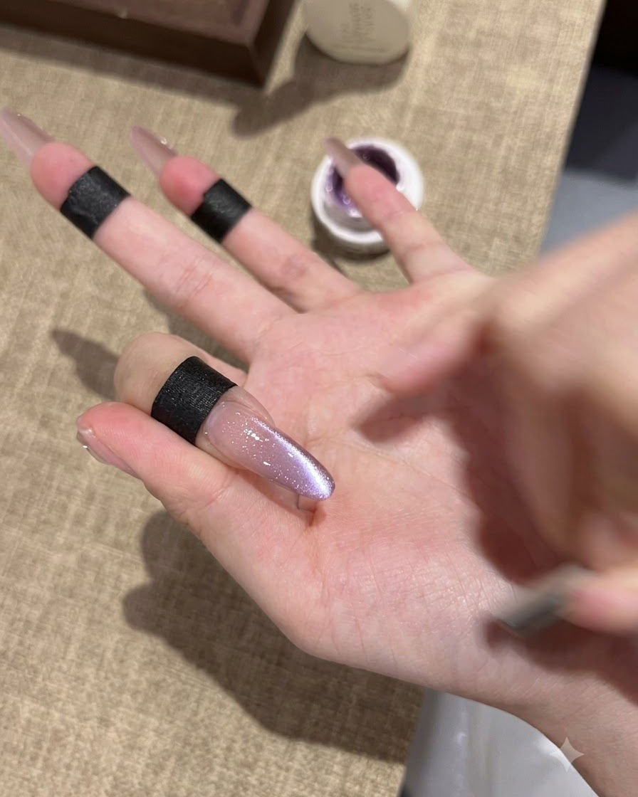 A close-up of an elongated almond nail showing a freshly set purple cat-eye gel polish with a shimmering reflective center.