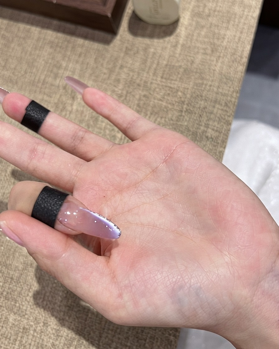 A brush applying a final glossy top coat over a purple ombre cat-eye nail with a fine silver glitter border.