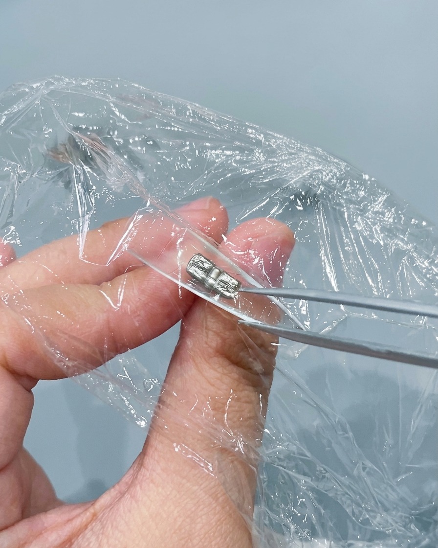 A pair of metal tweezers pinching and wrinkling plastic wrap pressed inside a clear nail tip.