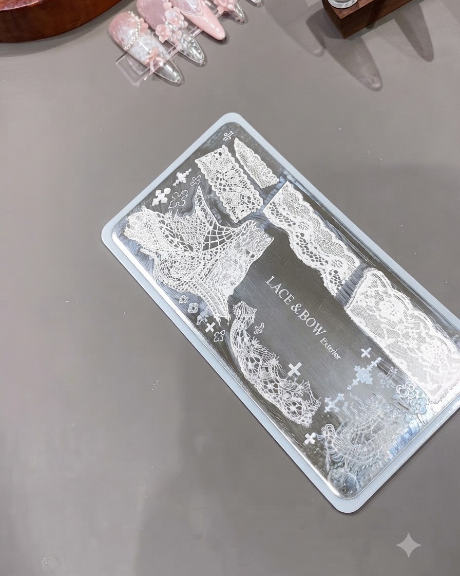 A clear silicone nail stamper positioned next to an engraved metal plate displaying intricate white lace patterns.