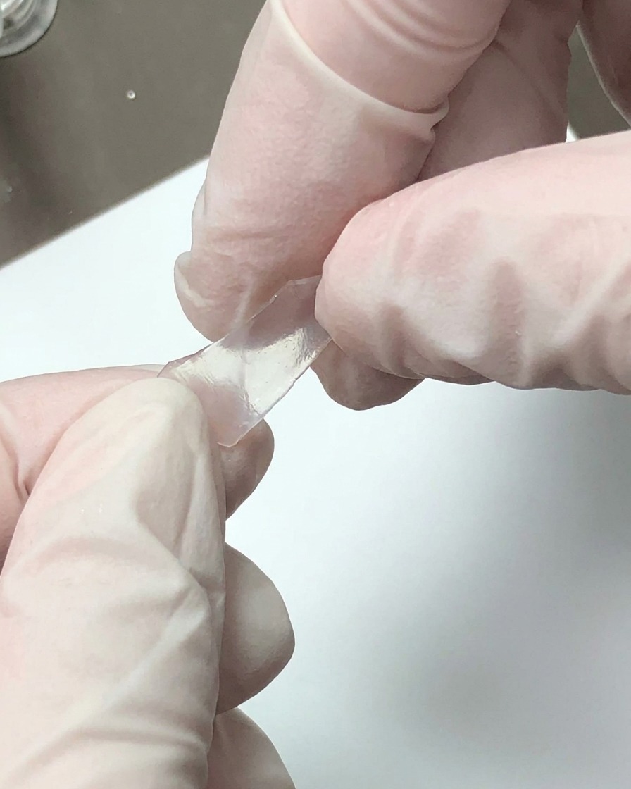 Gloved hands breaking a translucent decorative sheet into small fragments.