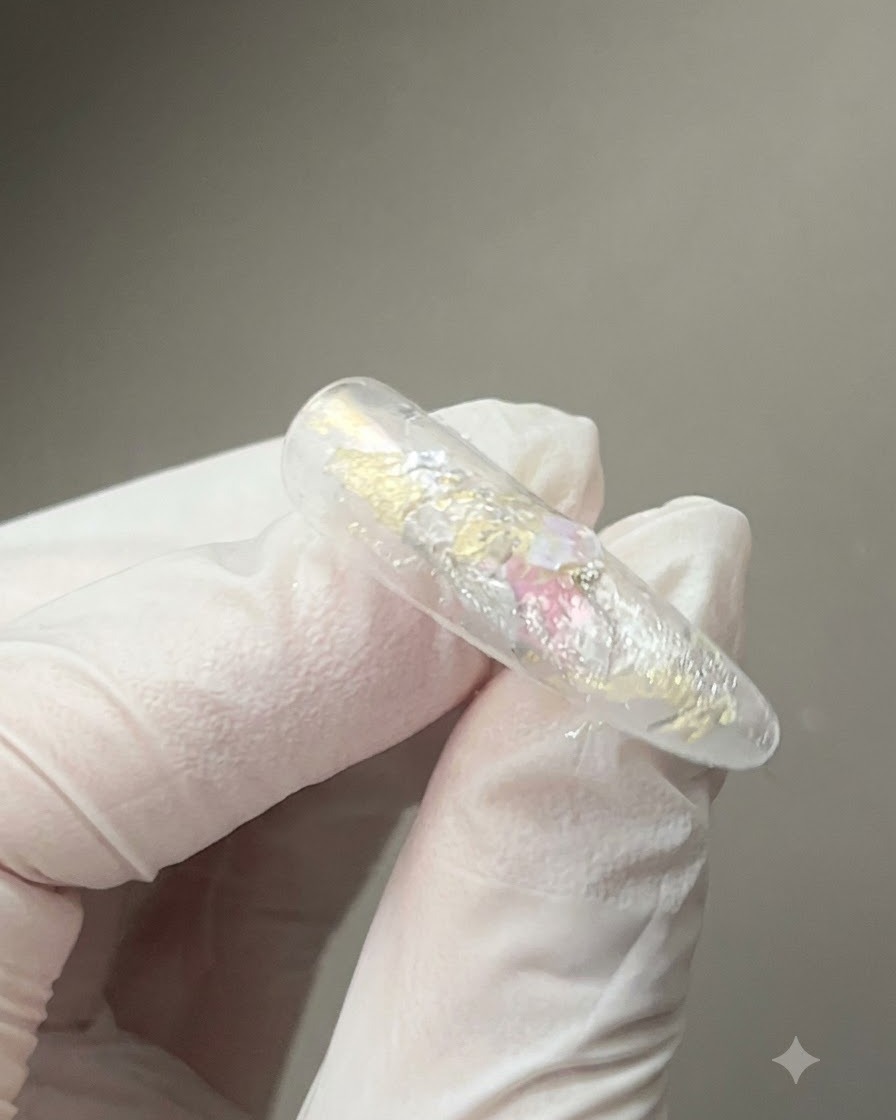 A magnet tool held closely over a glossy gel-coated nail to shape the reflective cat-eye magnetic particles.