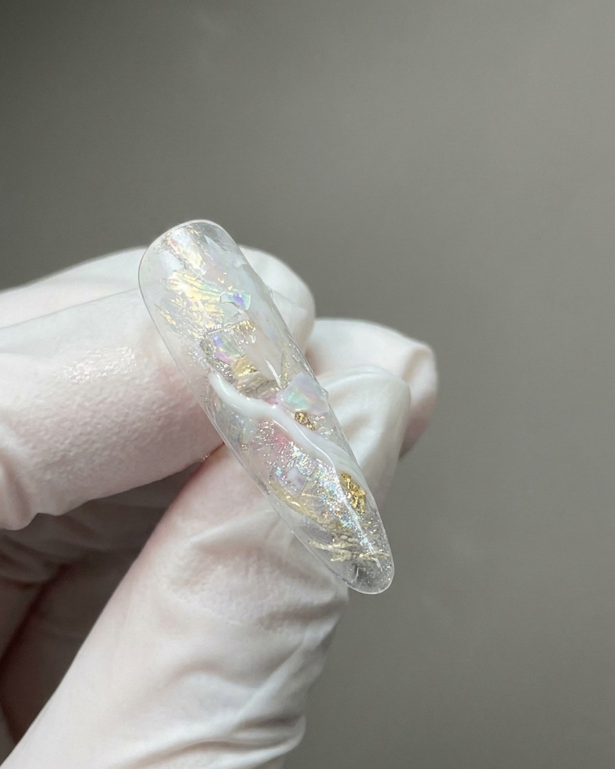 A close-up of a clear nail tip featuring embedded shimmering flakes and wisps of milky white marble detailing.