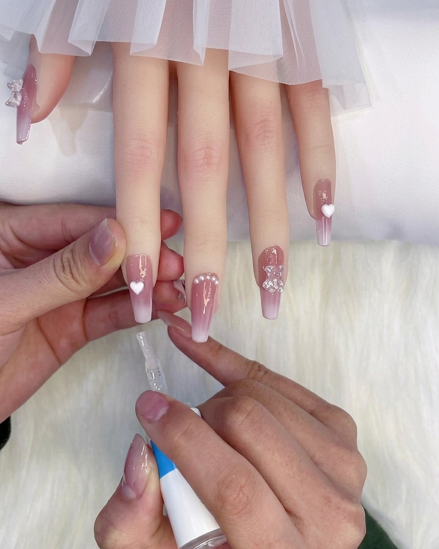 A bottle brush applying a glossy top layer over manicured fingers resting on a soft white background.
