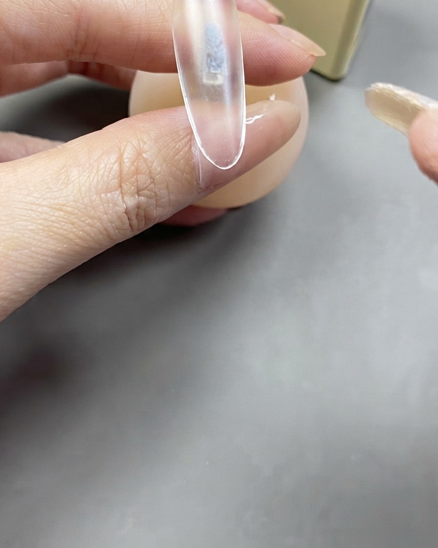 A brush applying a clear layer of base gel onto a clear nail extension.