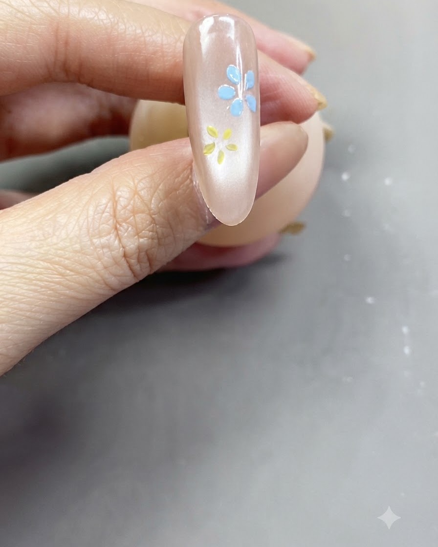 A close-up view of a completed soft pink flower painted onto a glossy nude-pink nail.
