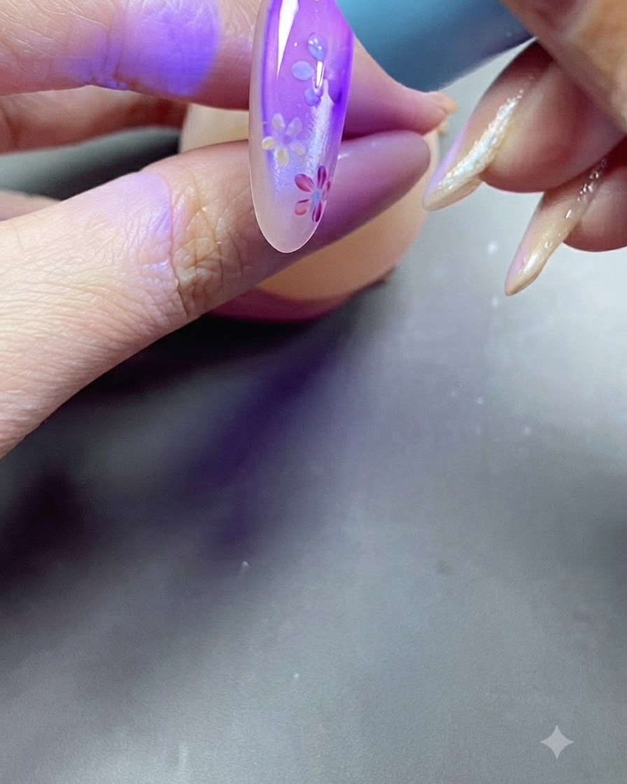 A hand placing a nail under a purple UV lamp light during the curing process.