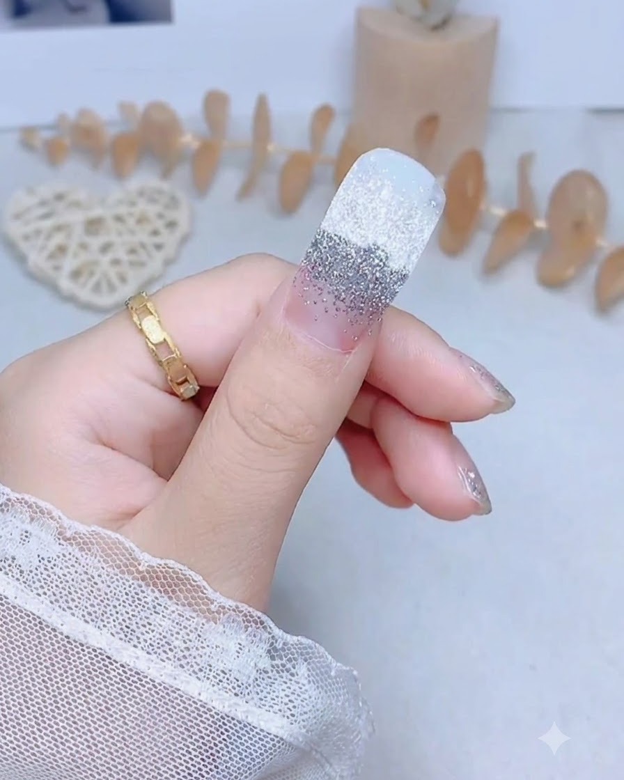 A thumb nail with a silver glitter sticker being pressed firmly down the center.