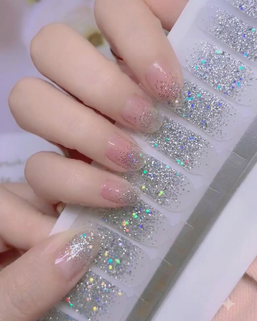 A thumb pressing firmly onto the cuticle area of a silver glitter nail wrap.