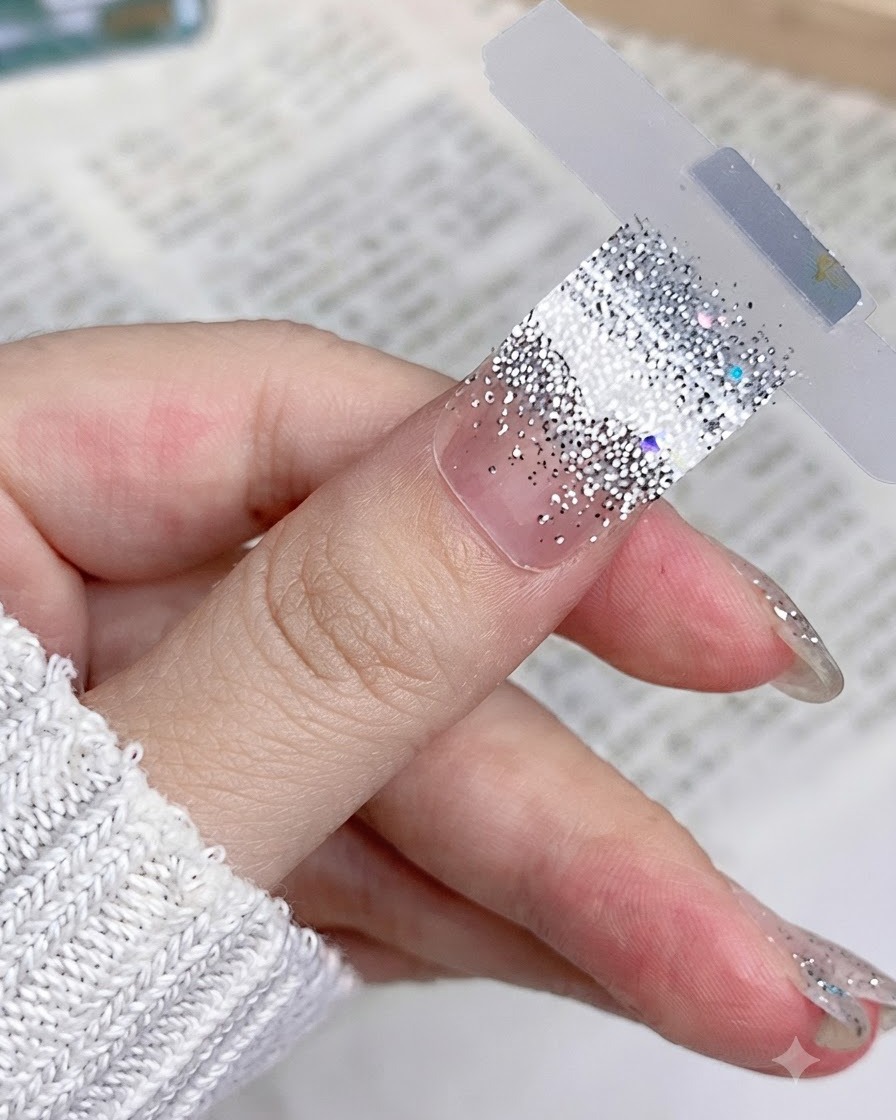 A close-up of a silver glitter nail sticker placed flat and smooth on a natural thumb nail.
