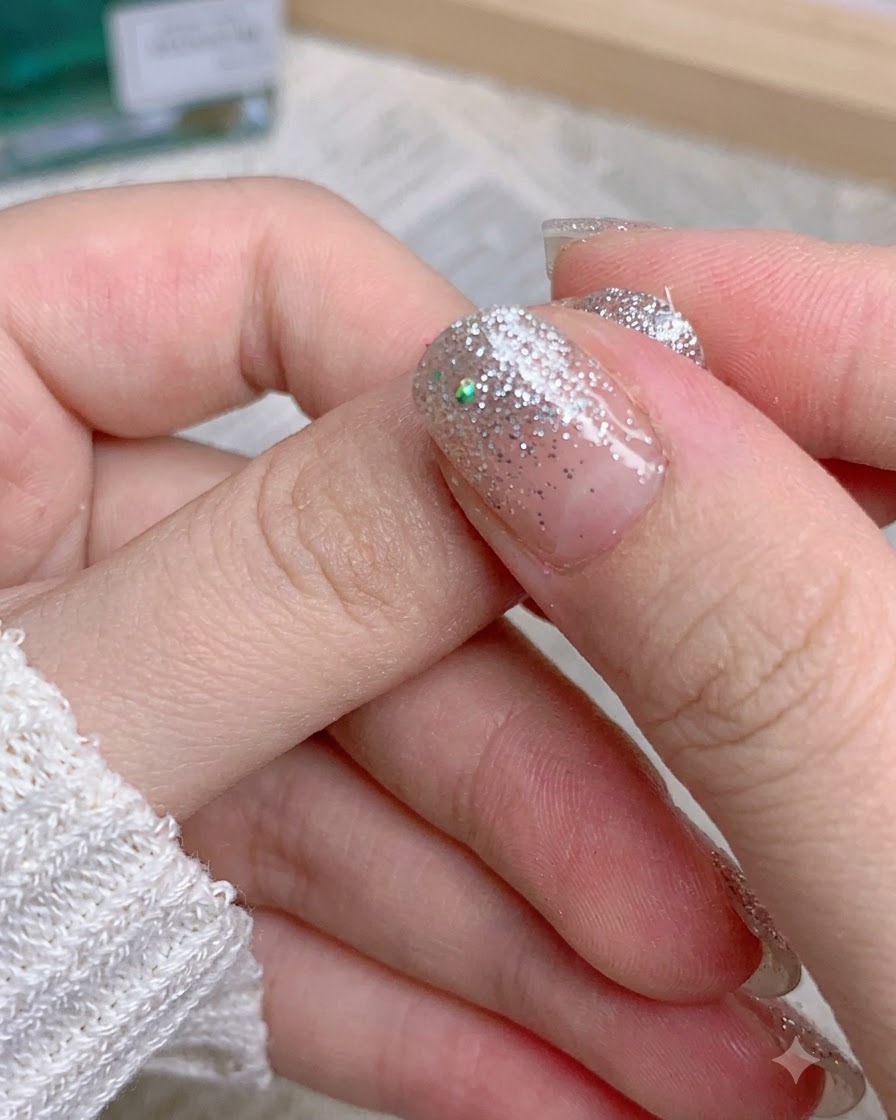Fingers peeling off the leftover glitter sticker edge from a manicured thumb.