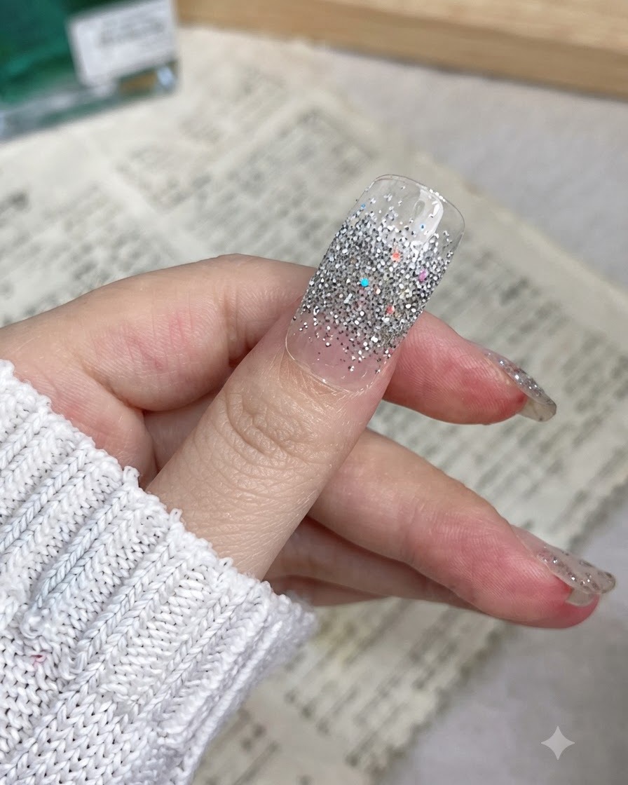 A close-up of a thumb with a silver glitter nail wrap smoothly applied from the cuticle to the edge.