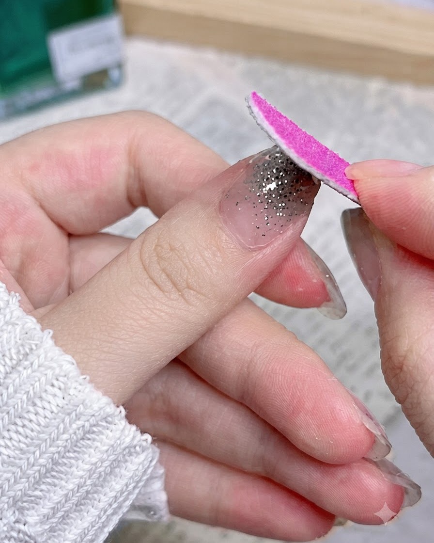 A pink nail file moving downward along the edge of a nail to remove excess wrap material.