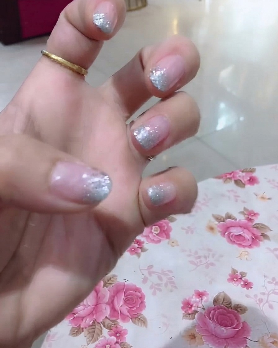 A close-up view of a hand highlighting the ring finger with glitter and fine word detailing.