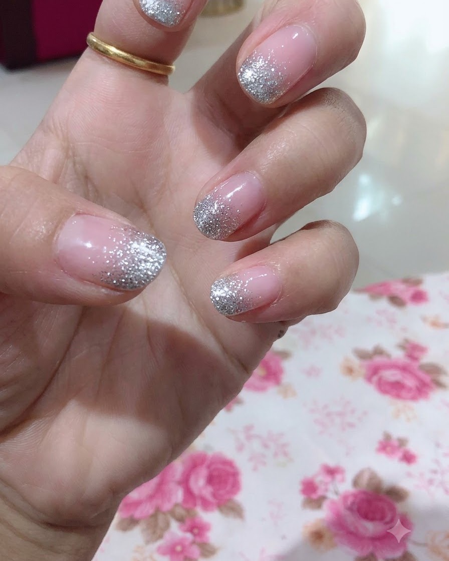 A close-up view of a hand highlighting the middle fingernail with a detailed silver glitter gradient design.
