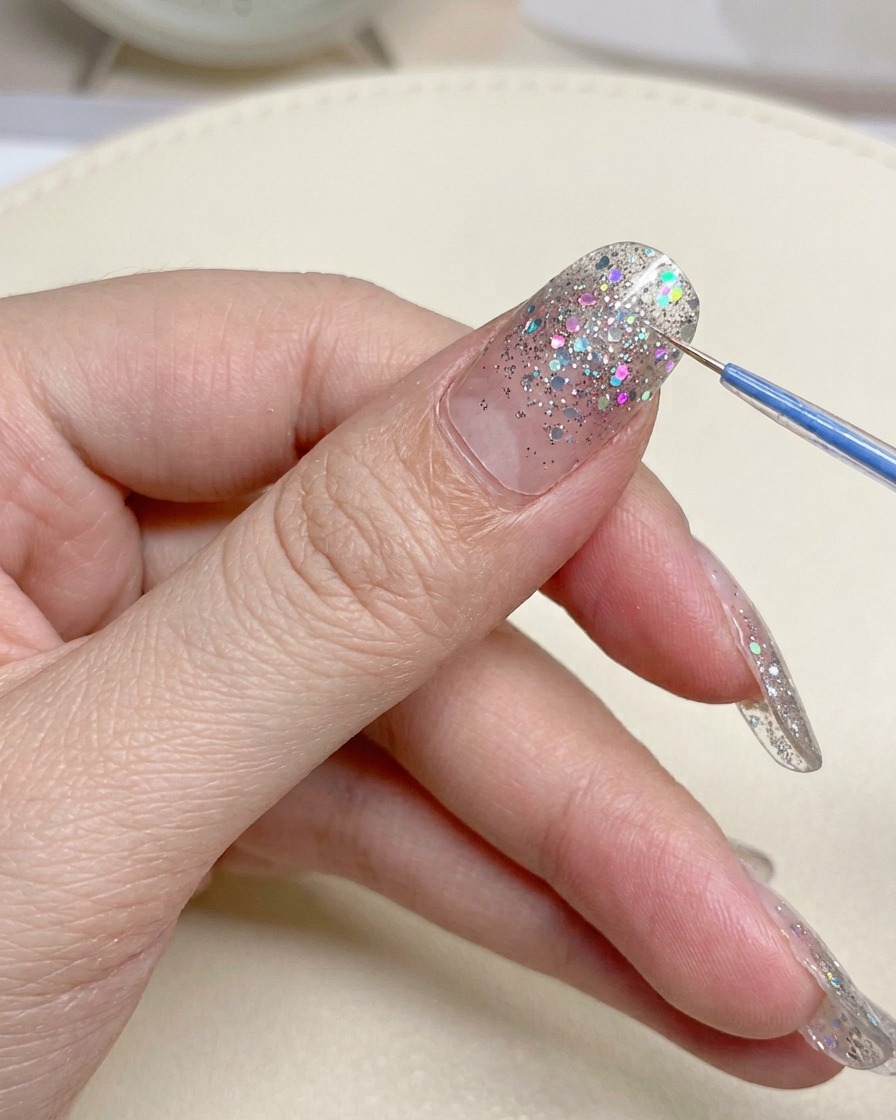 A close-up of metal nail clippers trimming the excess edge of a nail sticker.