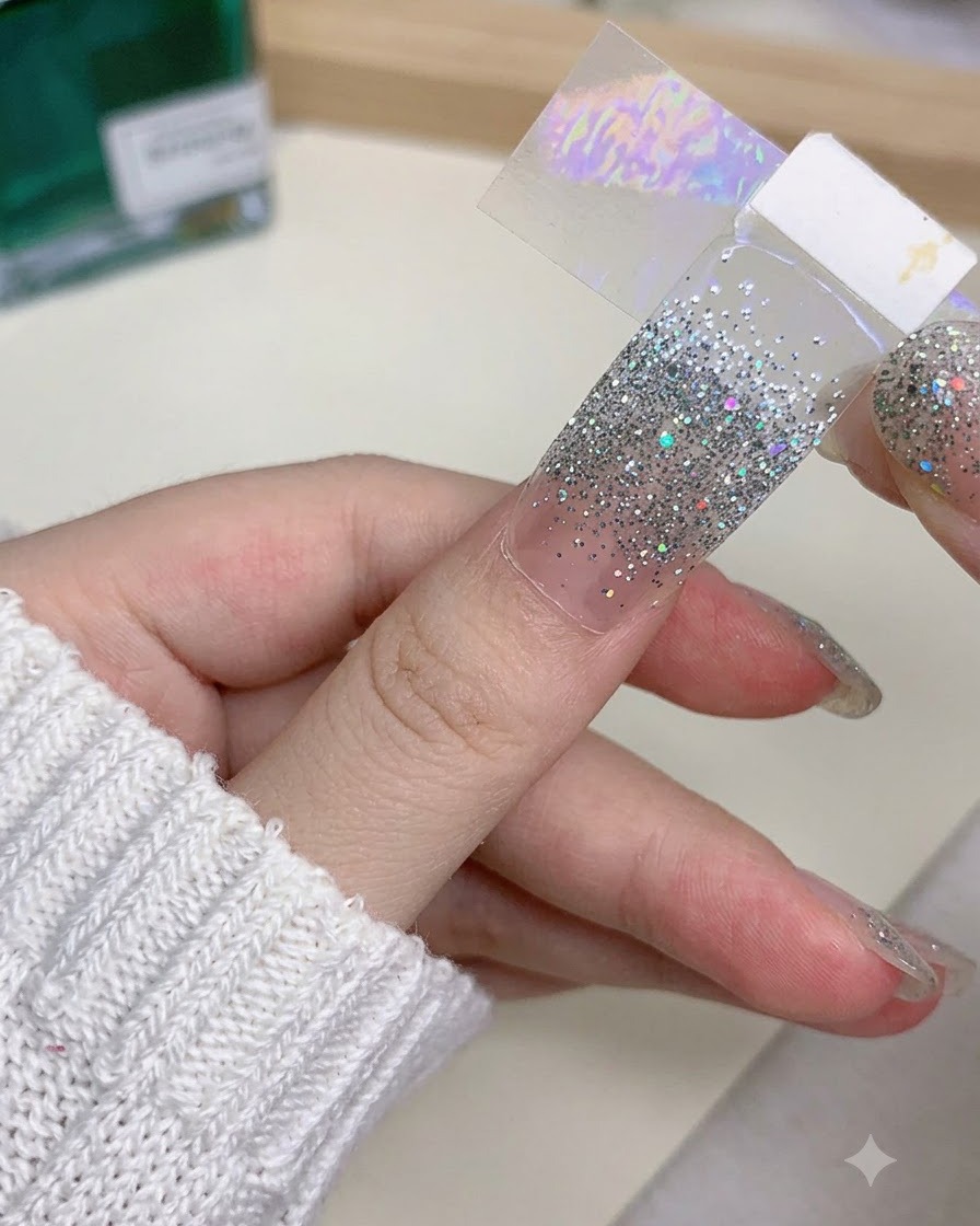 A close-up of a hand holding a false nail extension while carefully using a tool to adjust its edge.