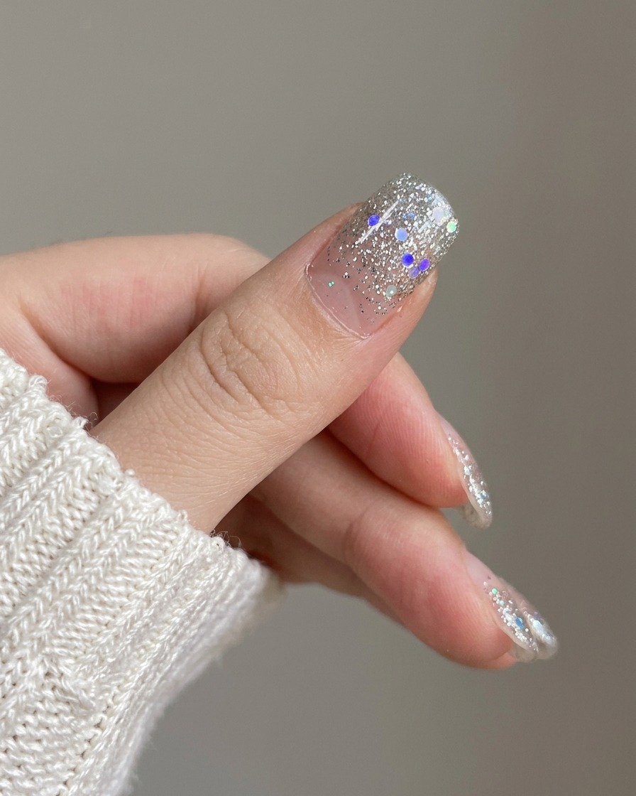 A close-up showcasing the newly applied silver glitter gradient nail on the index finger next to unpolished nails.