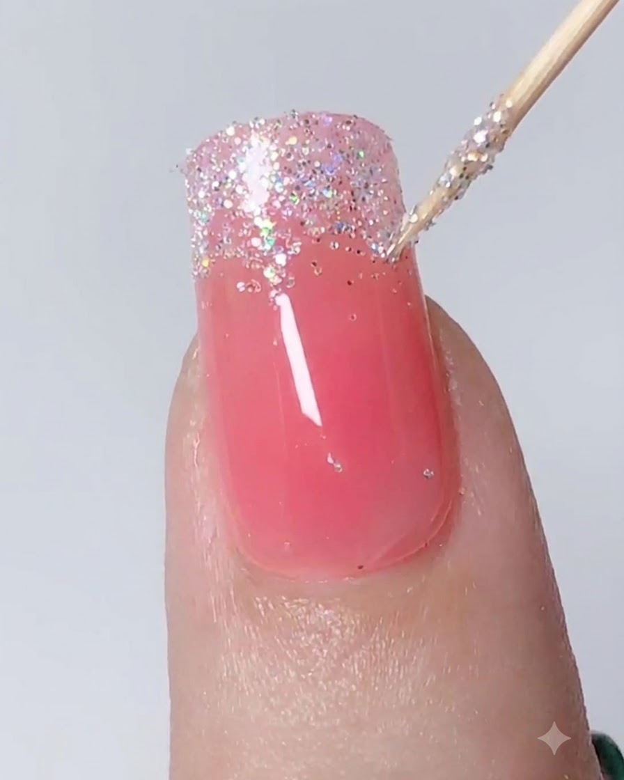 A detailing tool dabbing and pulling silver glitter downward to create an ombre gradient on a nail.