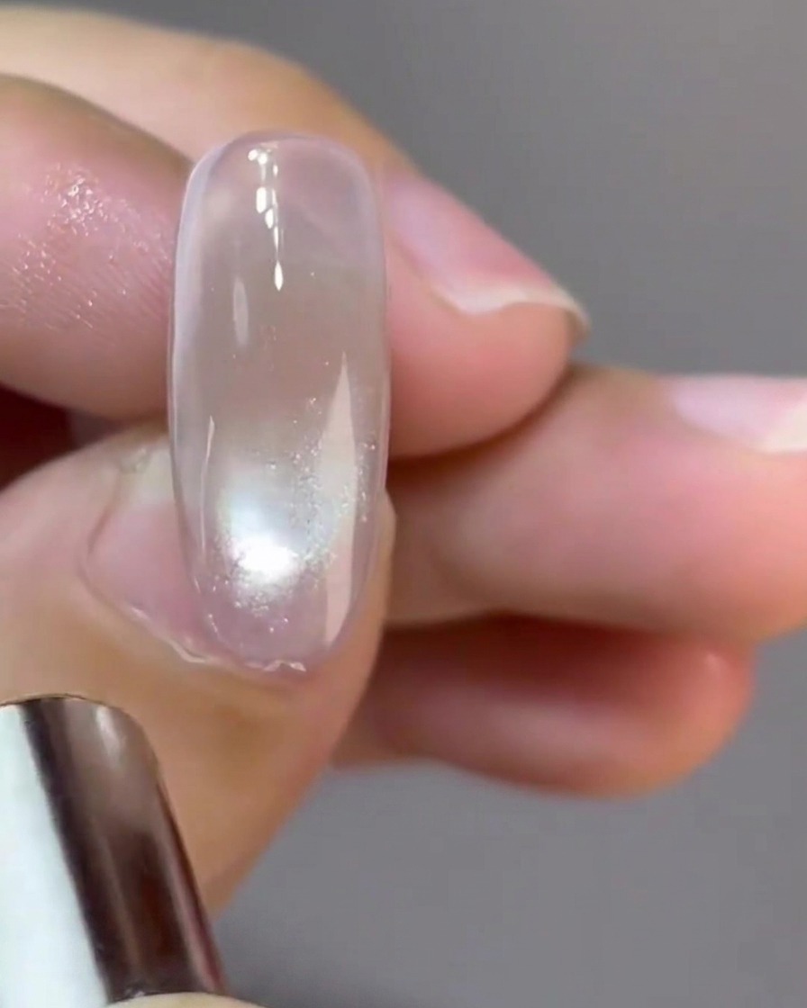 A small circular magnet shaping a reflective glass-ball cat-eye reflection on a nail.
