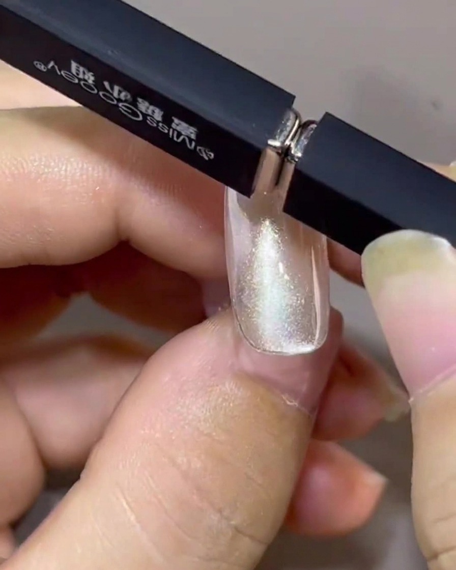 Two magnets held together at an angle above a fingernail, pulling the cat-eye polish into a floating band.