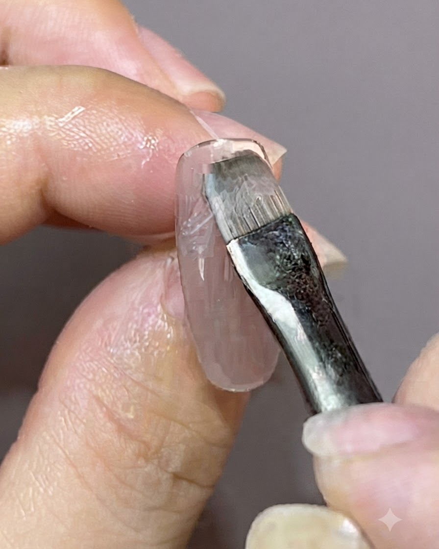 A detail brush applying a fresh coat of gel polish over a pre-existing magnetic nail design.