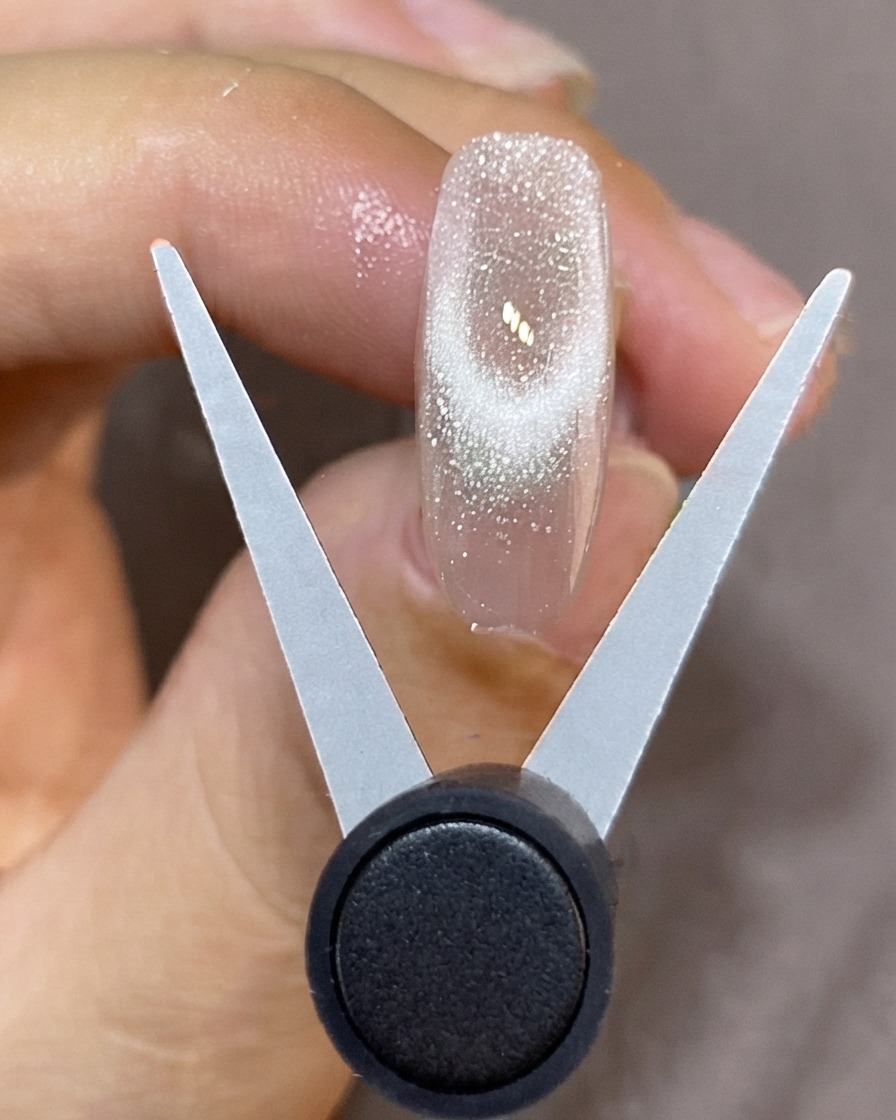 A V-shaped magnetic tool held over a translucent nail to create a sparkling French cat-eye tip.