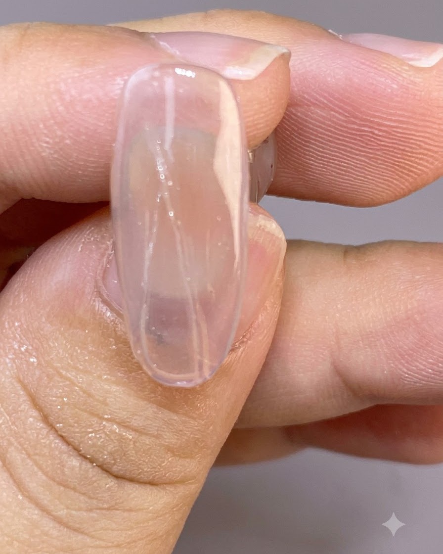 A close-up of a clear nail showing fine, delicate painted feather lines drawn across the wet surface.