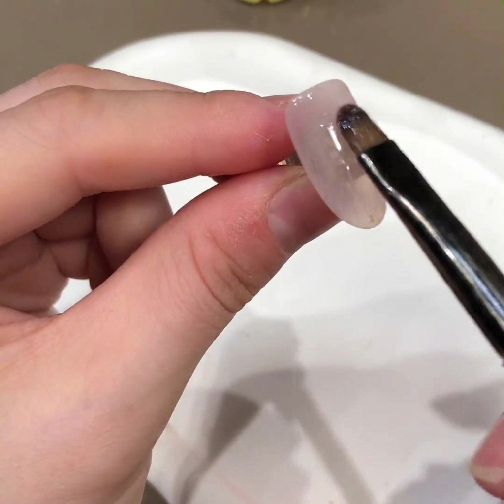 A nail brush applying a nude pink gel base color onto the surface of an artificial nail.