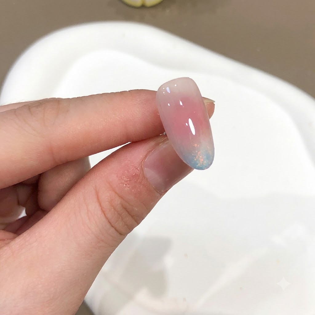 A close-up of a nail showing a pink and blue aurora powder effect with a high-gloss finish.