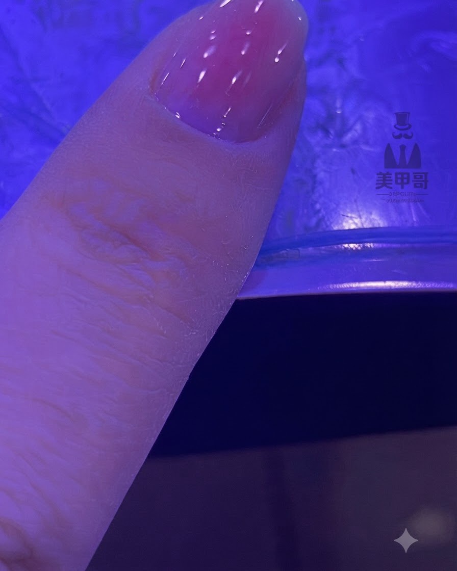 A fingernail with a blended pink gradient curing under a UV/LED lamp.