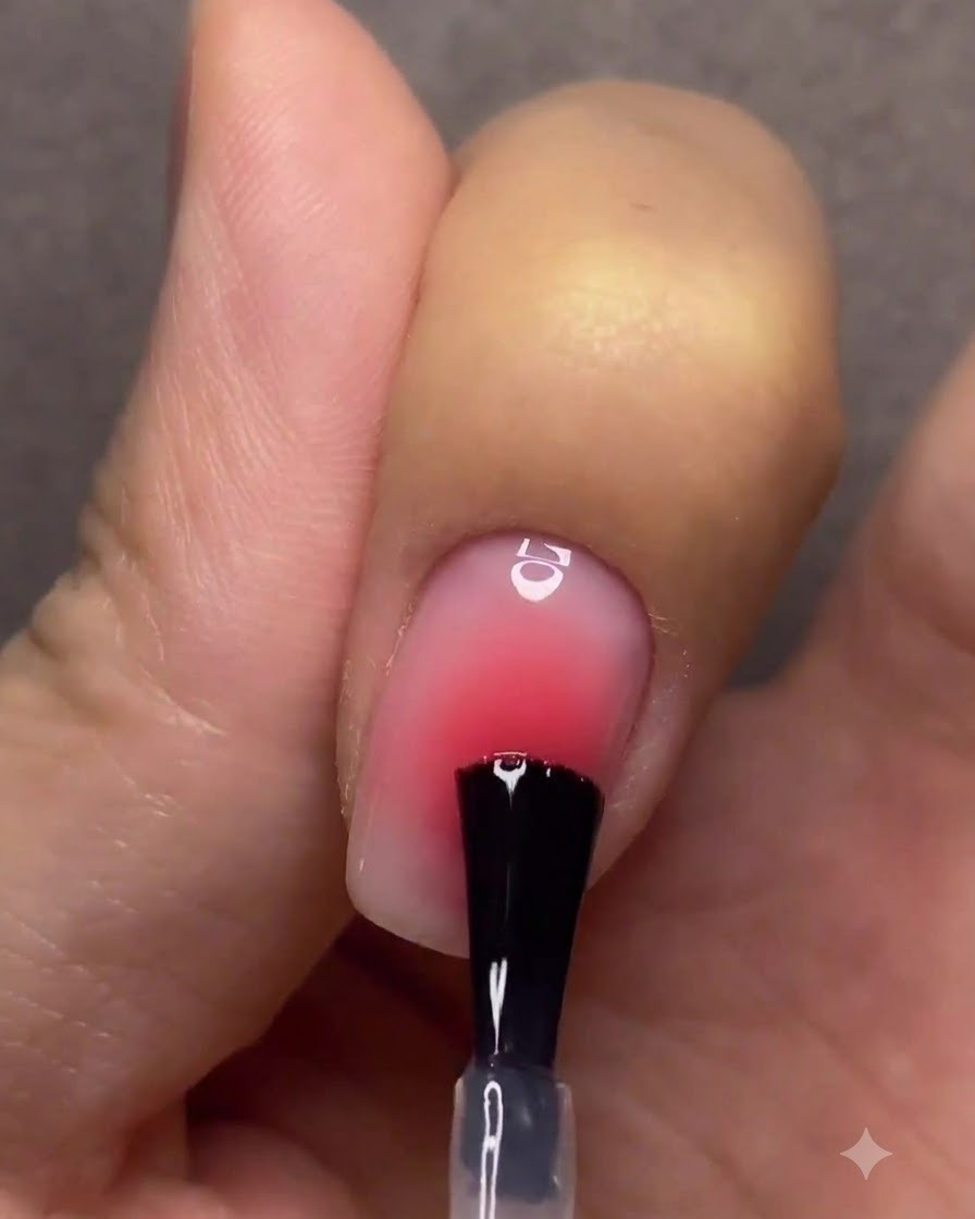 A hand with finished gradient nails curing under a pink UV/LED nail lamp.