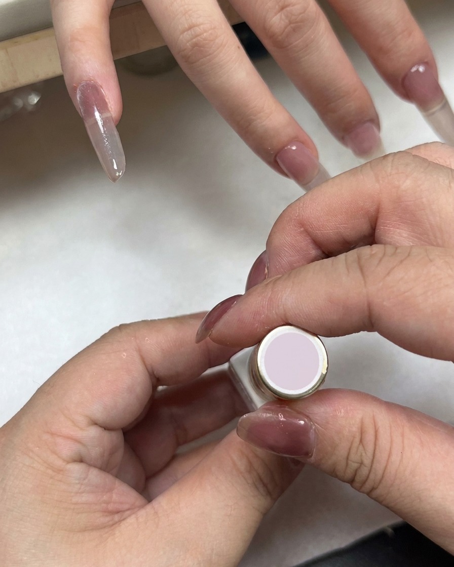 A nail polish bottle with a light pink cap being held near a hand with gradient nails.