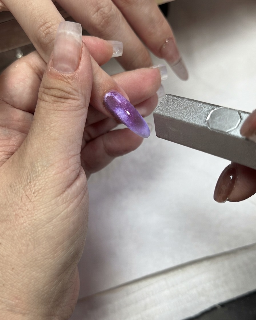 A magnetic wand being used over a purple cat eye color block applied to an index finger.