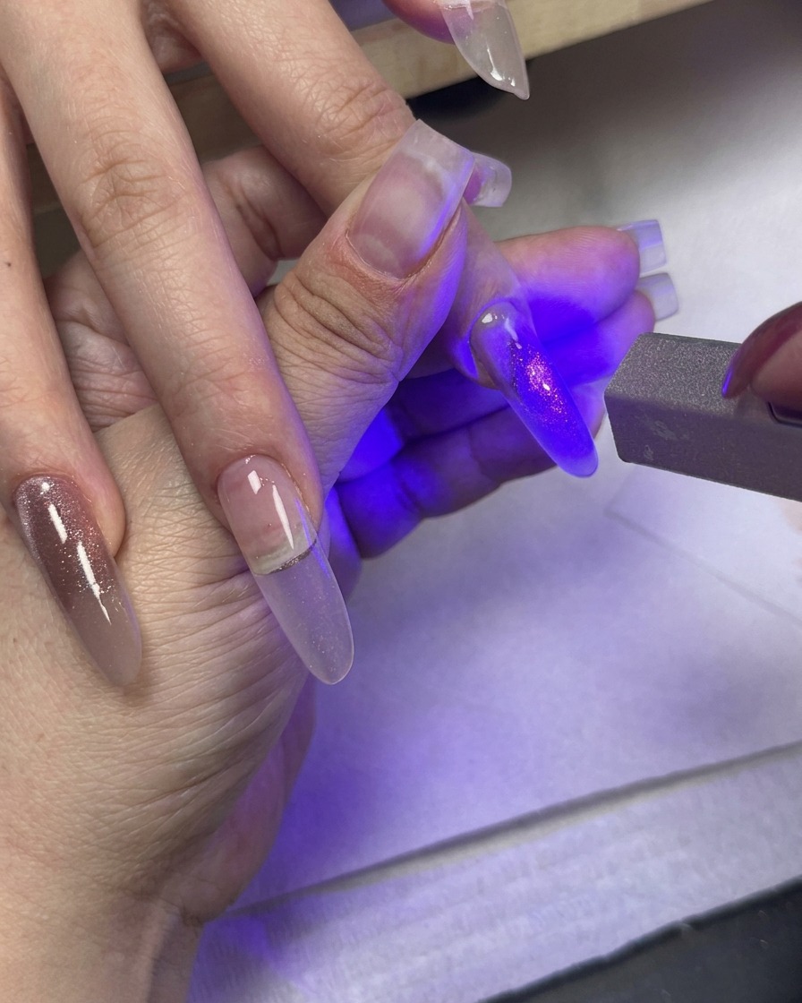 A UV light curing a painted nail while other fingers with gradient cat-eye gel rest nearby.