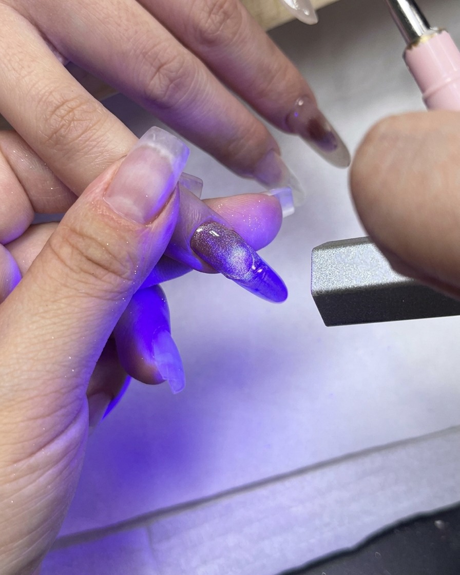 A UV/LED curing light pointed directly at the middle finger showcasing the textured French tip.