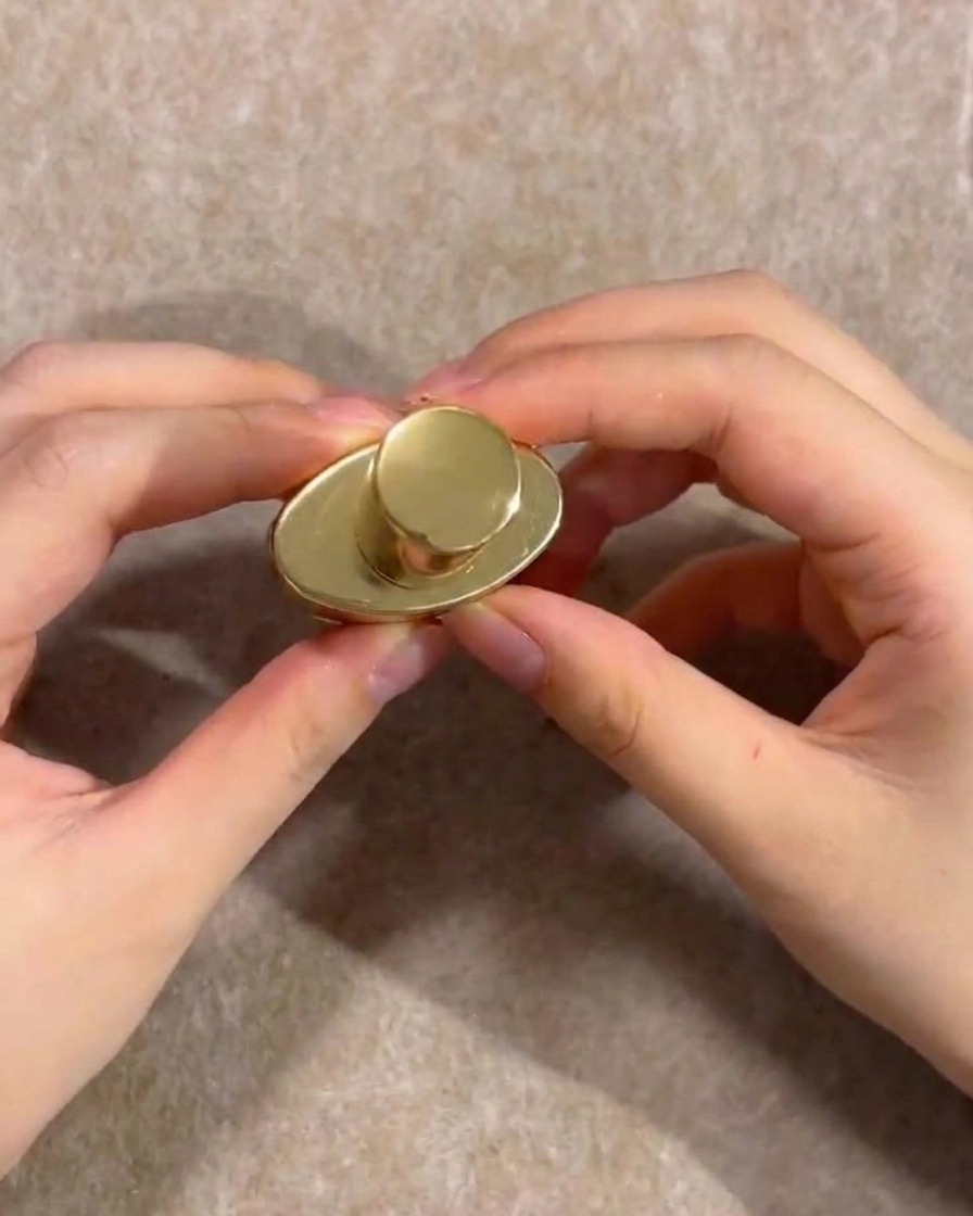 Hands holding the gold cap of a nude gel polish bottle.