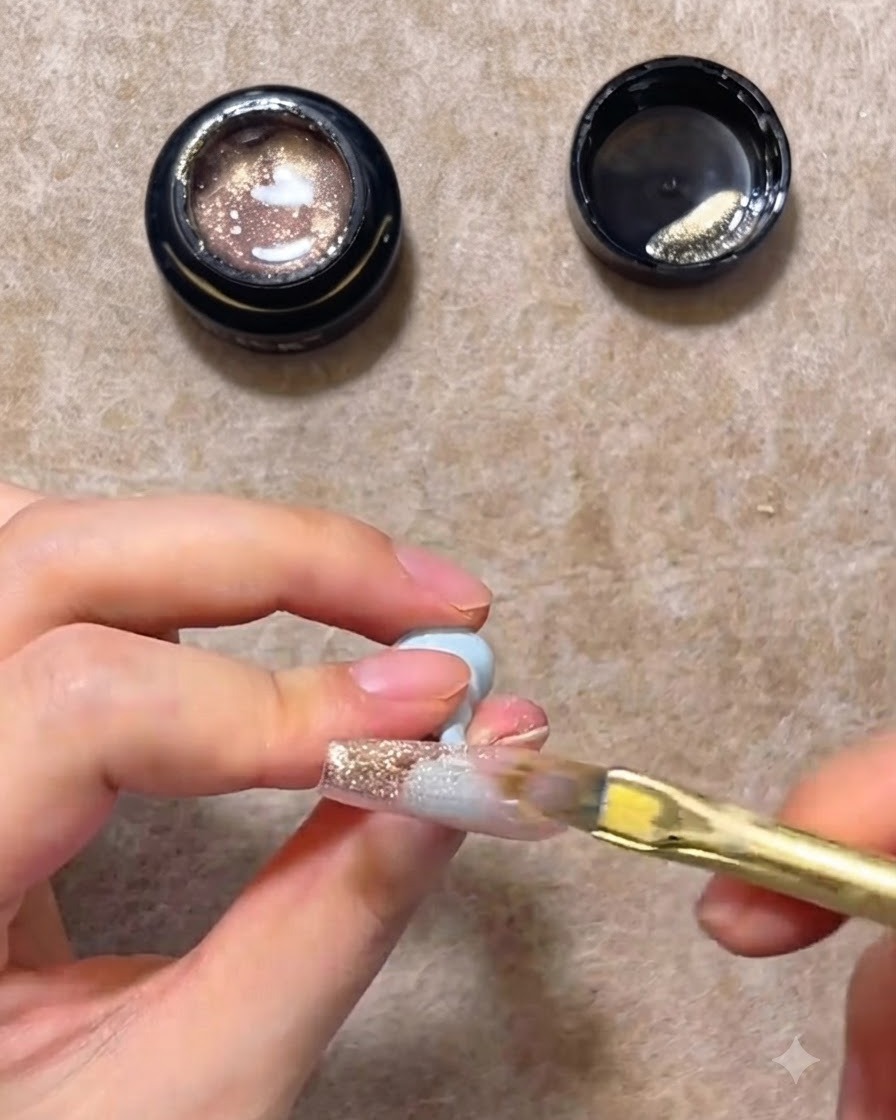 A flat nail brush sweeping pink gold cat eye gel down a clear nail extension to create a gradient.
