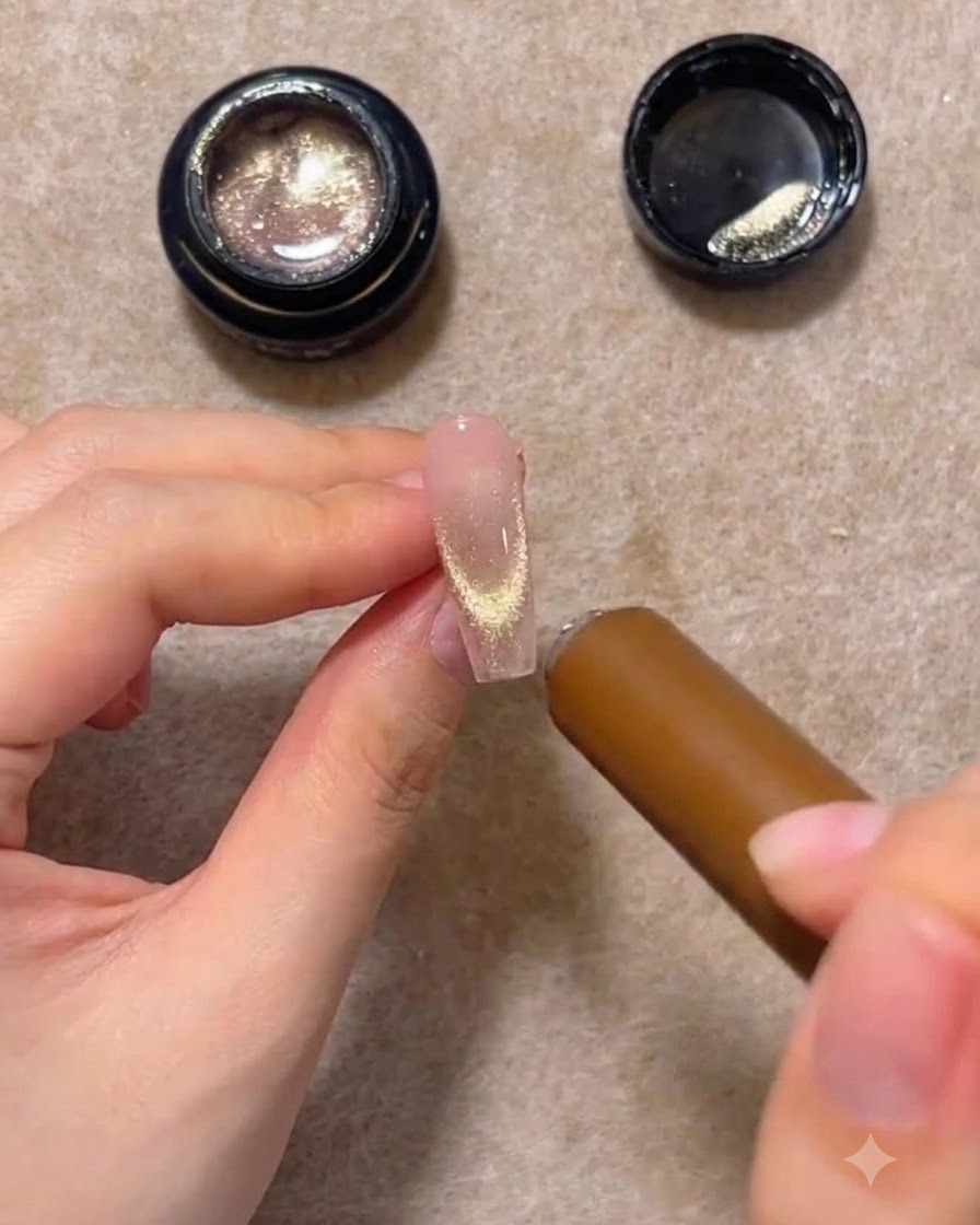 A cylindrical magnetic wand hovering near the tip of a nail extension, gathering the glitter into a glowing U-shape.