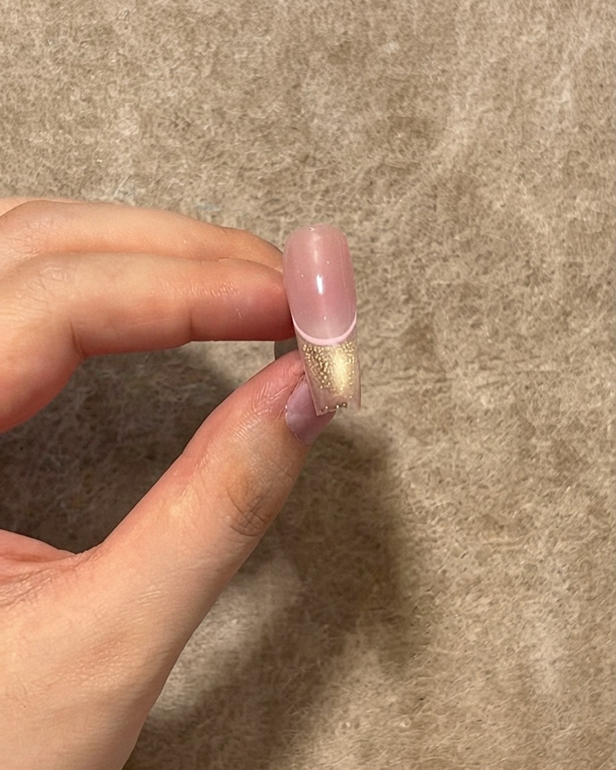 A finished nail showing a glossy top coat layer applied over the pink line, cat eye tip, and blush center.