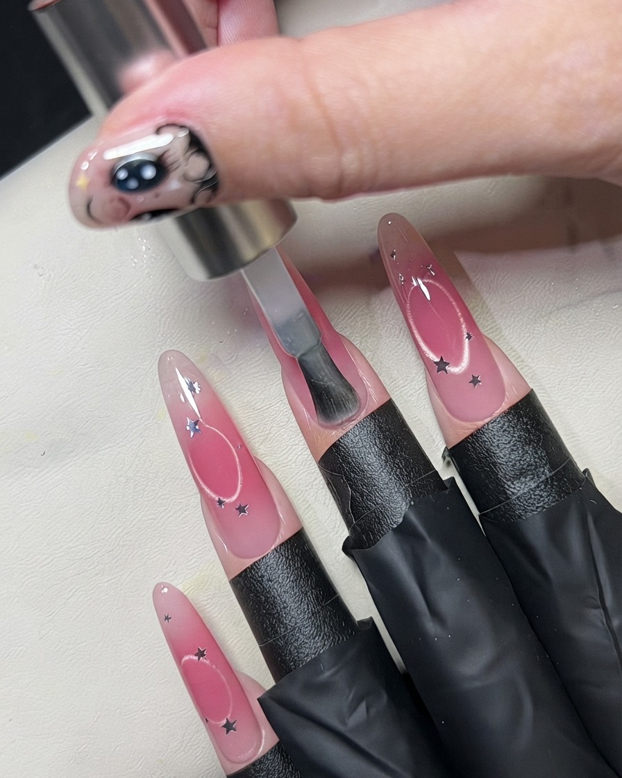 A brush applying a clear coat over a decorated nail with star sequins.
