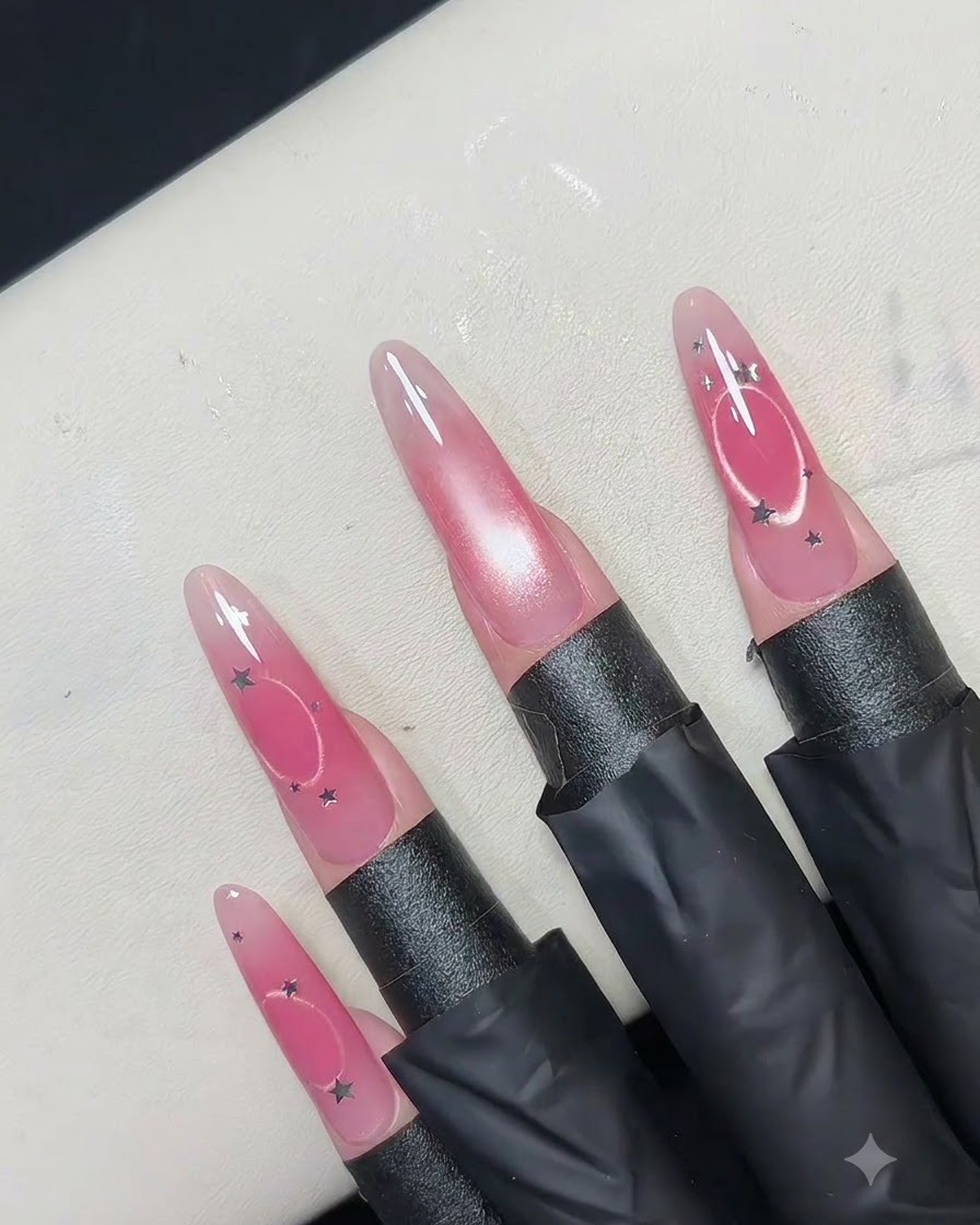 A hollow circular magnet tool held above a pink nail to push magnetic shimmer outward into a ring.