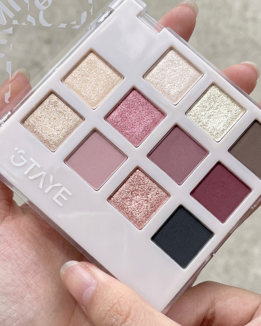 A silicone tool scooping peach pink gel from a multi-compartment eyeshadow and gel palette.