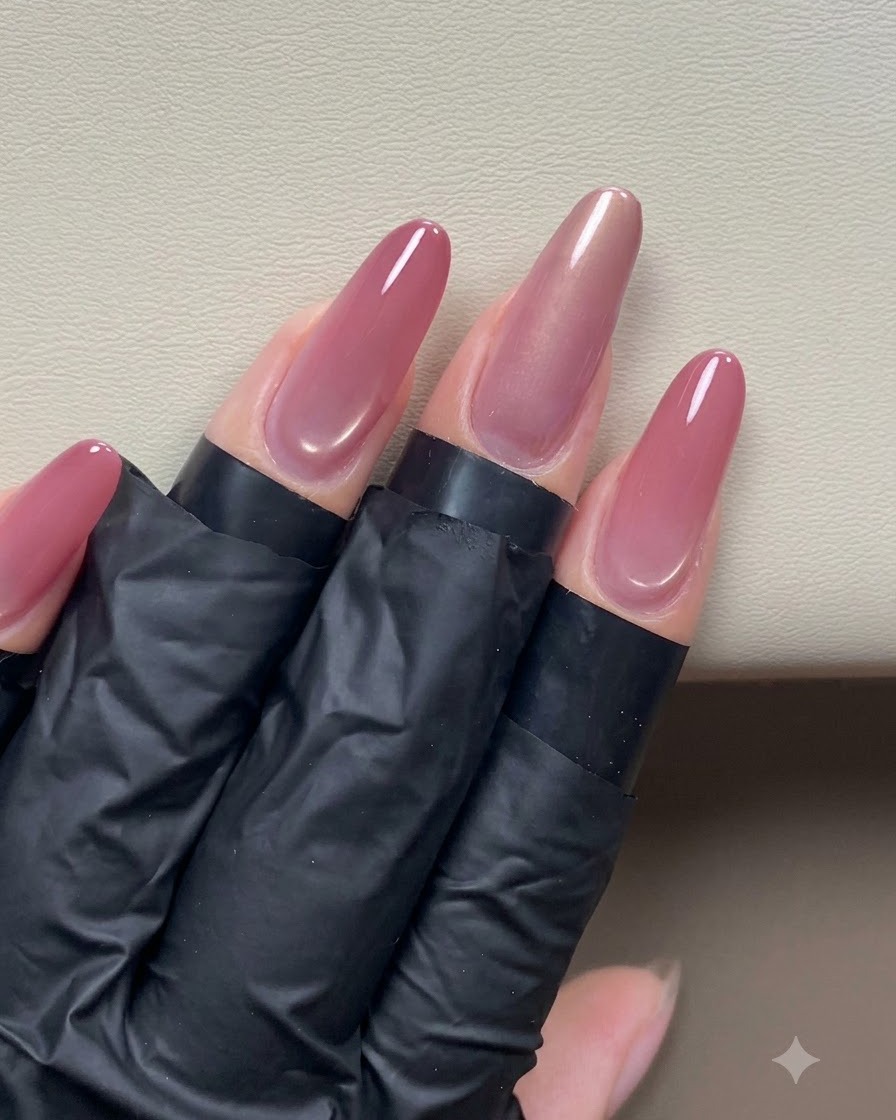 A hand holding a pen magnet near a glossy pinkish-gold cat-eye nail to shape a side light effect.