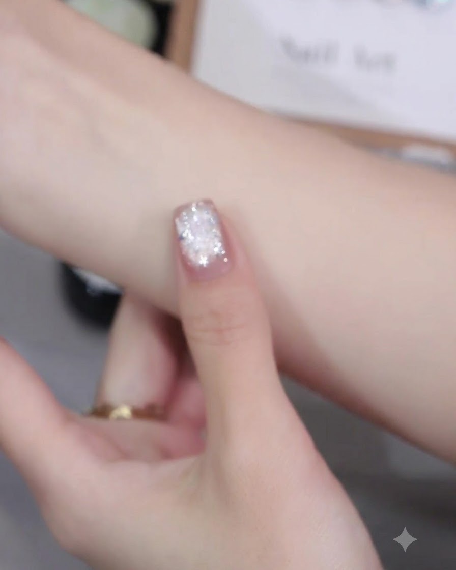 A nail brush applying pink cat-eye gel polish evenly onto a fingernail surface.