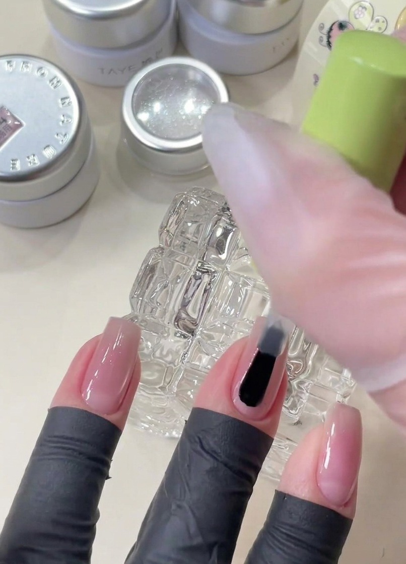 A brush applying clear base gel onto a nail before placing decorative star sequins.